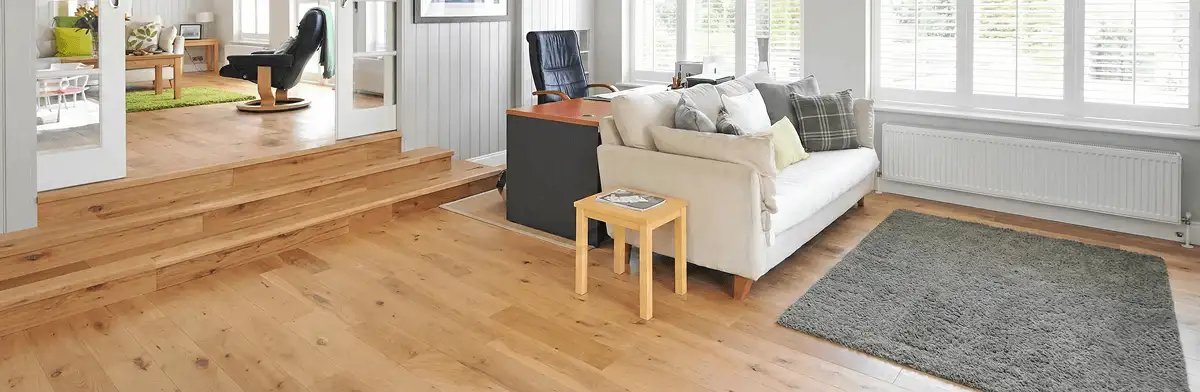 A modern living room with professionally installed laminate flooring, a beige sofa, a small side table, a gray rug, and large windows with white shutters in Dallas, TX